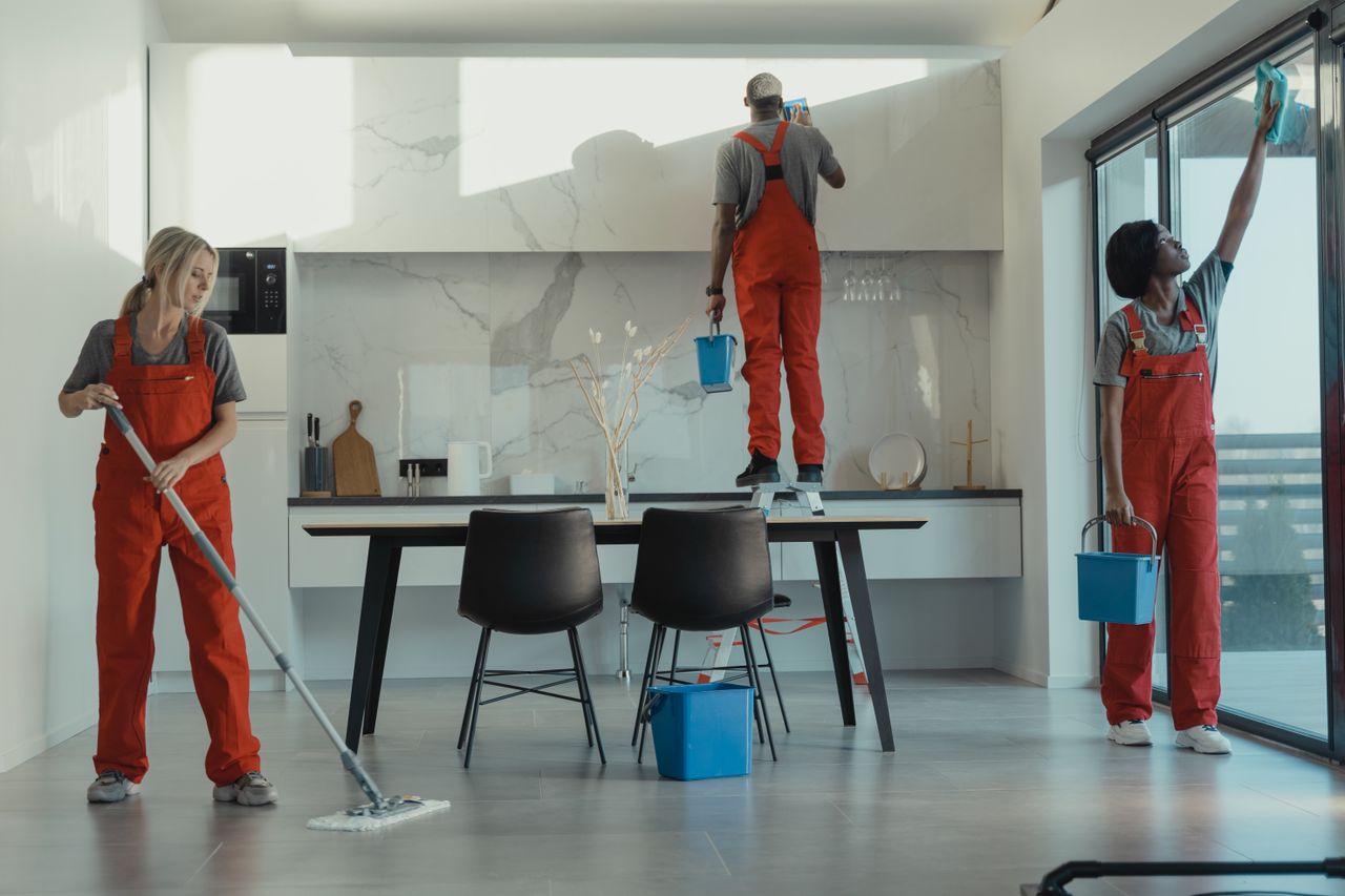 who-we-are Group of cleaners in red uniforms mopping and wiping glass in a modern dining room.